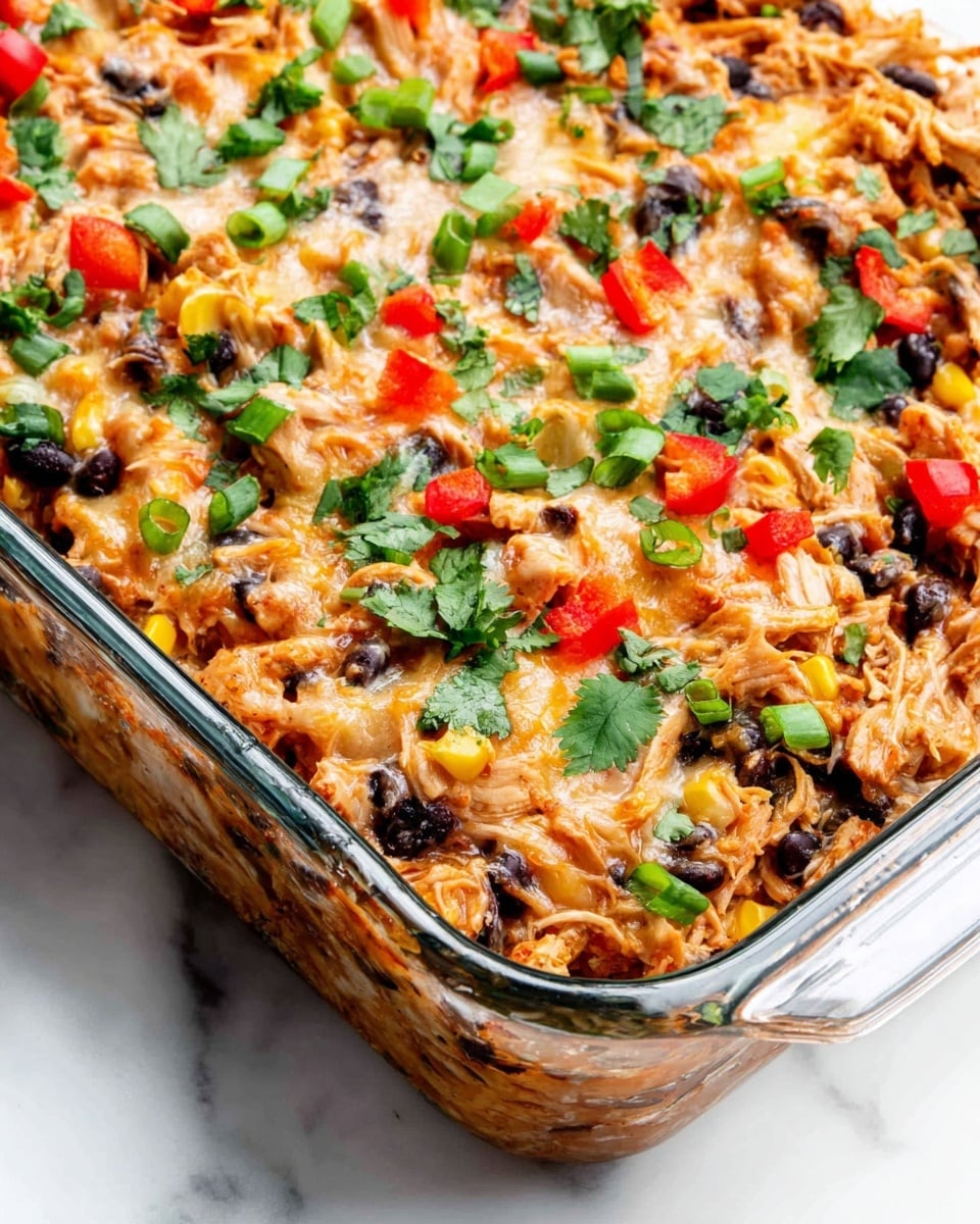 A close-up view of a baked casserole in a clear glass dish with a mix of shredded chicken, black beans, and corn, visible as the base layer with a warm golden-brown melted cheese layer on top, dotted with bright red bell pepper pieces and chopped green onions. Fresh green cilantro leaves are scattered over the whole casserole, adding a fresh color contrast. The glass dish is set against a white marbled surface. photo taken with an iphone --ar 4:5 --v 7