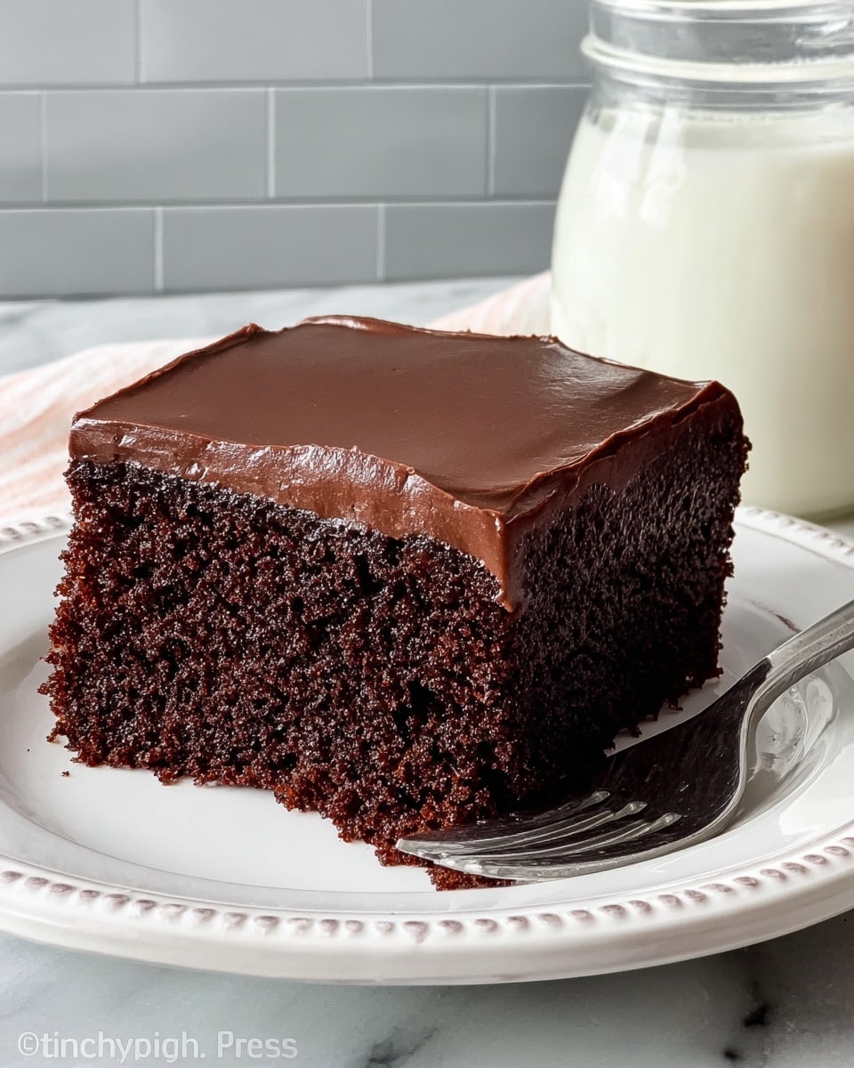 A single piece of chocolate cake sits on a white plate with a decorative rim, placed on a white marbled surface. The cake has two layers: a thick, dark brown, moist chocolate sponge at the bottom, and a smooth, shiny chocolate frosting layer on top. The frosting has a glossy texture and covers the entire top surface evenly, with slightly rounded edges. A silver fork with four prongs rests on the right side of the plate. A glass jar filled with white cream is partially visible in the background, placed against a light gray tiled wall. Photo taken with an iphone --ar 4:5 --v 7