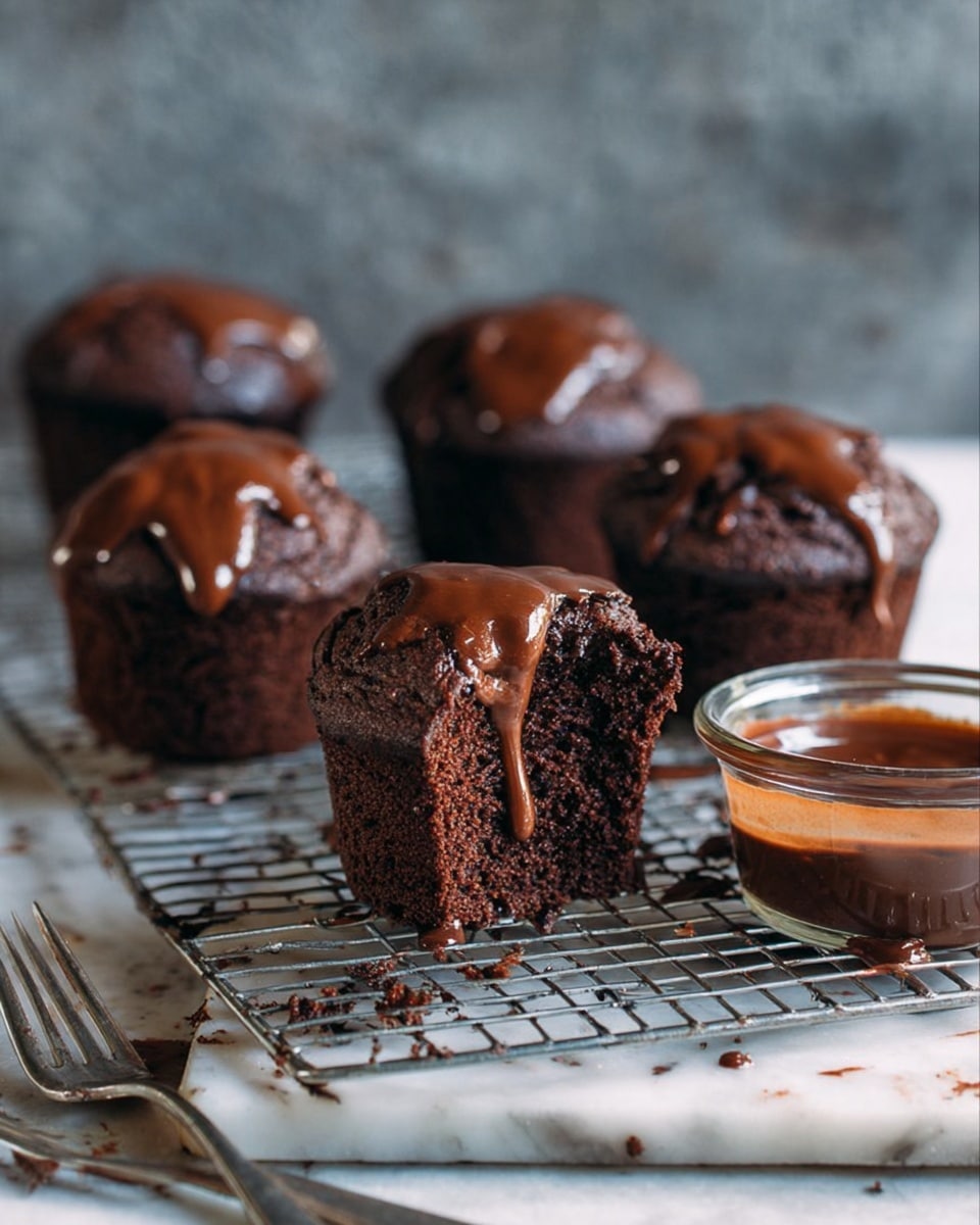 The image shows five rich chocolate muffins arranged on a wire cooling rack with a white marbled surface underneath. One muffin is cut in half and placed in front, revealing a moist, dark brown crumb inside. Thick, glossy chocolate sauce is dripping from the top of the cut muffin, creating a shiny contrast against the dark cake. To the right of the muffins, there is a small clear container filled with smooth chocolate sauce, and some of it is smeared on the edge. Two metal forks lie on the white marbled surface near the bottom left corner. The background is blurred, focusing on the muffins and sauce. Photo taken with an iphone --ar 4:5 --v 7