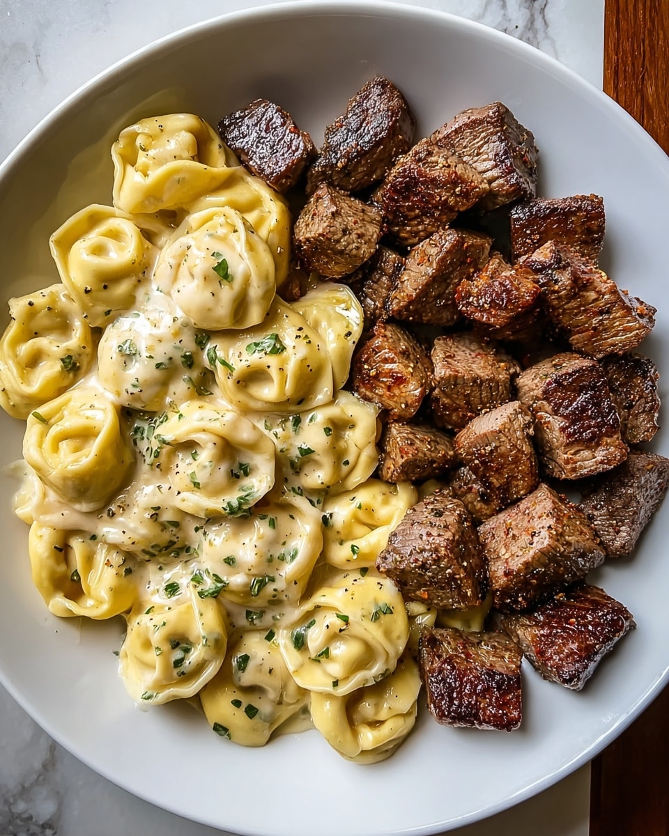 A white plate is filled with two main parts: on the left side, creamy tortellini pasta coated in a smooth, pale yellow sauce, sprinkled with chopped green herbs and black pepper, each tortellini showing a soft, rounded shape with delicate folds; on the right side, a pile of rich brown, seared beef cubes with a slight char on the edges, their texture looking juicy and tender, slightly glistening with a light sauce beneath; the dish sits on a white marbled surface. photo taken with an iphone --ar 4:5 --v 7