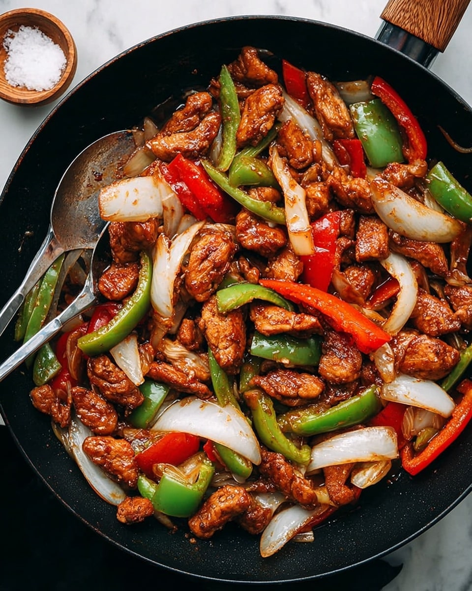 The image shows a black pan filled with cooked chicken stir-fry. The dish has three main visible layers: tender chunks of brown, saucy chicken pieces, thick slices of white onion, and large pieces of bright red and green bell peppers scattered evenly throughout. The mixture looks glossy and well-coated with sauce, giving it a juicy, slightly shiny texture. A pair of silver chopsticks rest on the side of the pan, and a small wooden bowl with coarse salt is nearby, all set against a white marbled textured surface. photo taken with an iphone --ar 4:5 --v 7