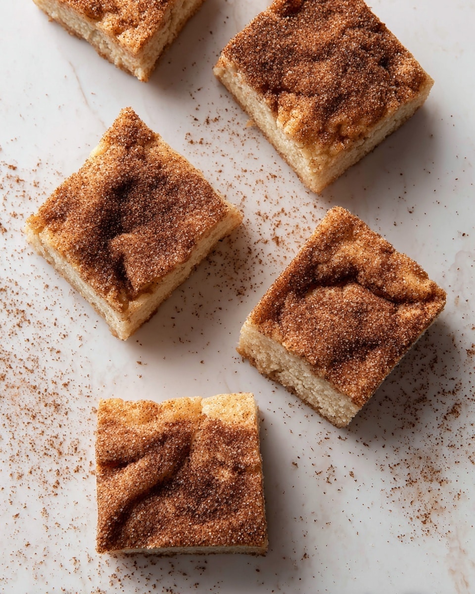 Five pieces of square cinnamon sugar cake are spread on a white marbled surface. Each cake piece has a rough top layer covered in a mix of brown cinnamon and white sugar crystals, giving a grainy texture. The inside layer shows a soft, light beige texture with a slightly crumbly look. Cinnamon powder is lightly dusted around the cakes, adding a rustic feel. The pieces vary slightly in shape, with one piece having a small crack on top. Photo taken with an iphone --ar 4:5 --v 7